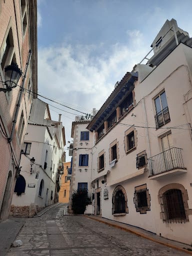 Carrer de la Davallada, Sitges: a cobbled old-town corner with cream townhouses, iron balconies and a stepped lane climbing behind